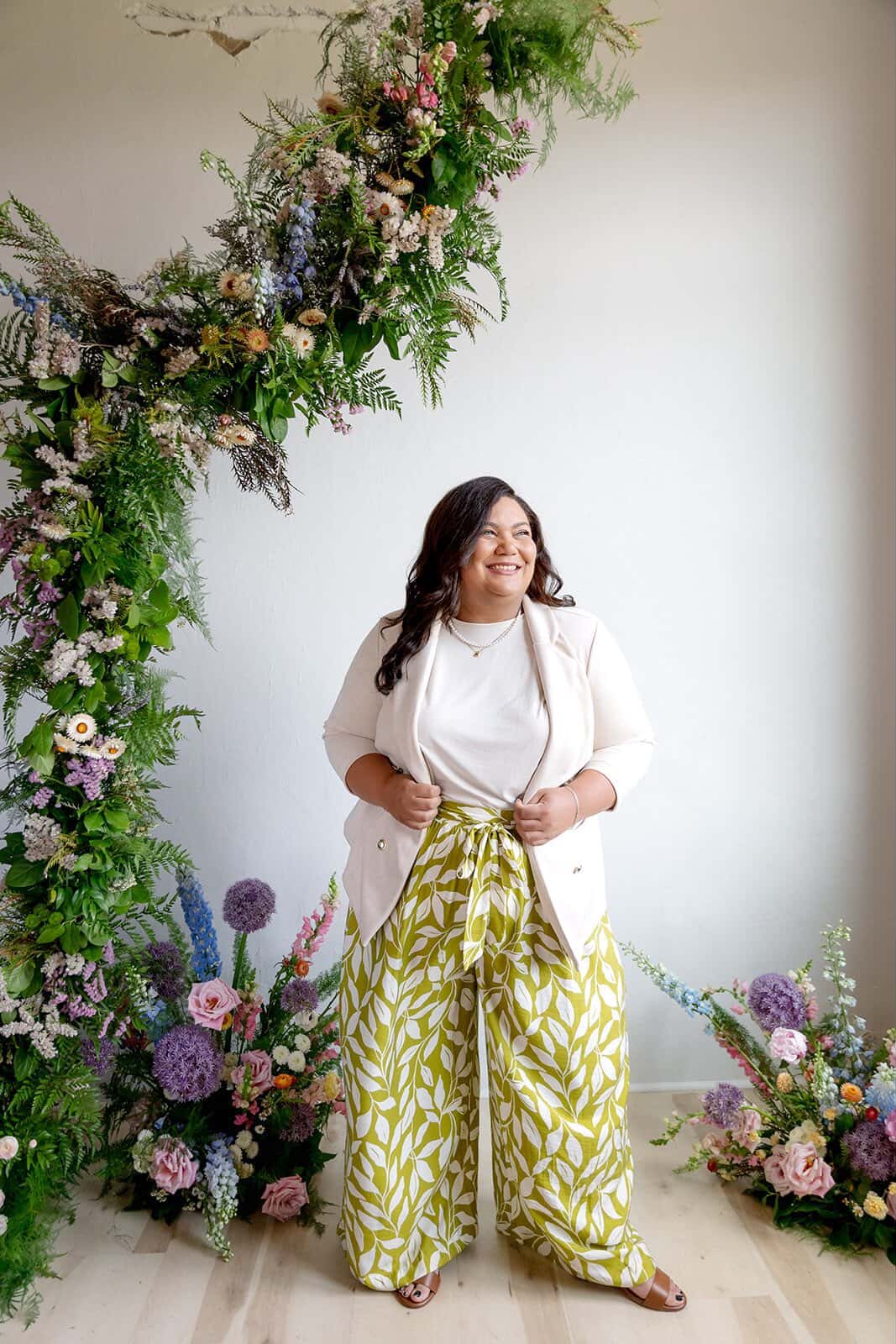 The woman behind Love and Whimsy Events stands with some flower arrangements smiling