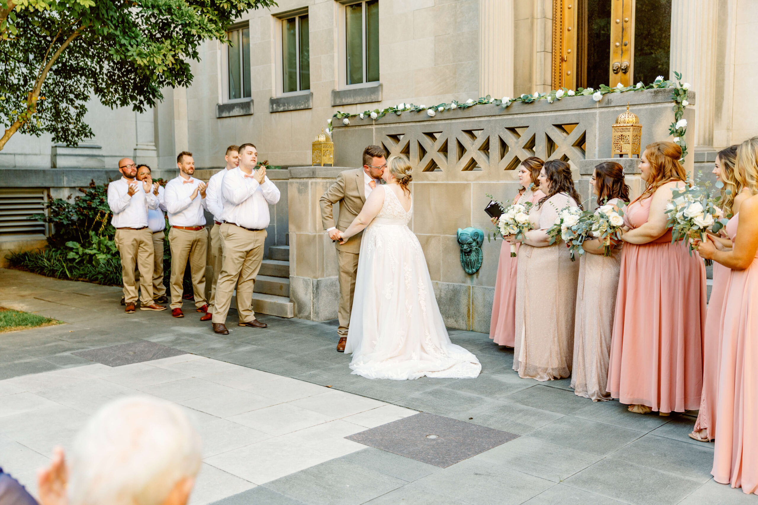 A bride and groom kiss to end their garden ceremony with wedding party watching and clapping