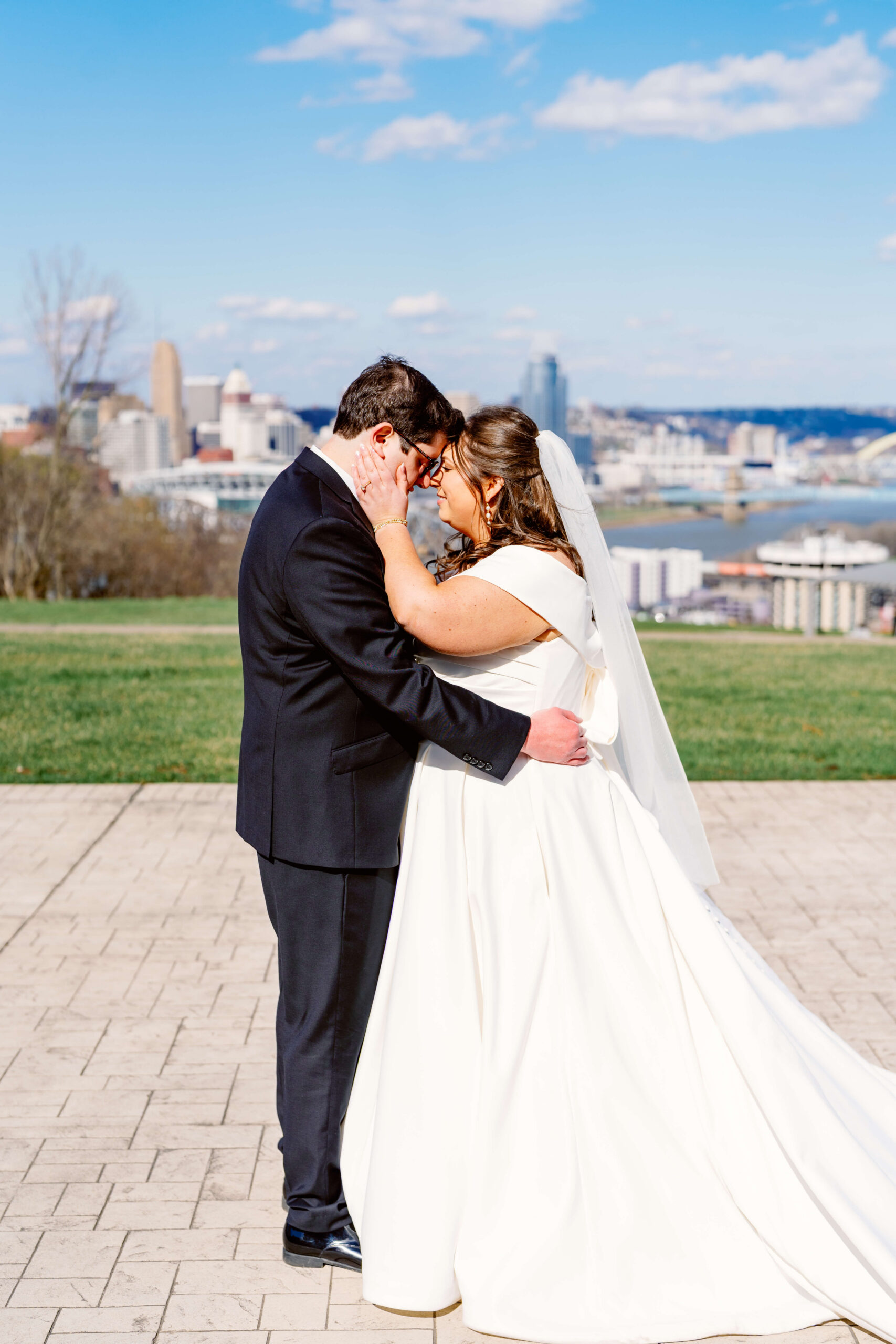 A bride and groom cuddle touching foreheads on a patio overlooking the city from across the river at one of the cincinnati wedding venues with a view