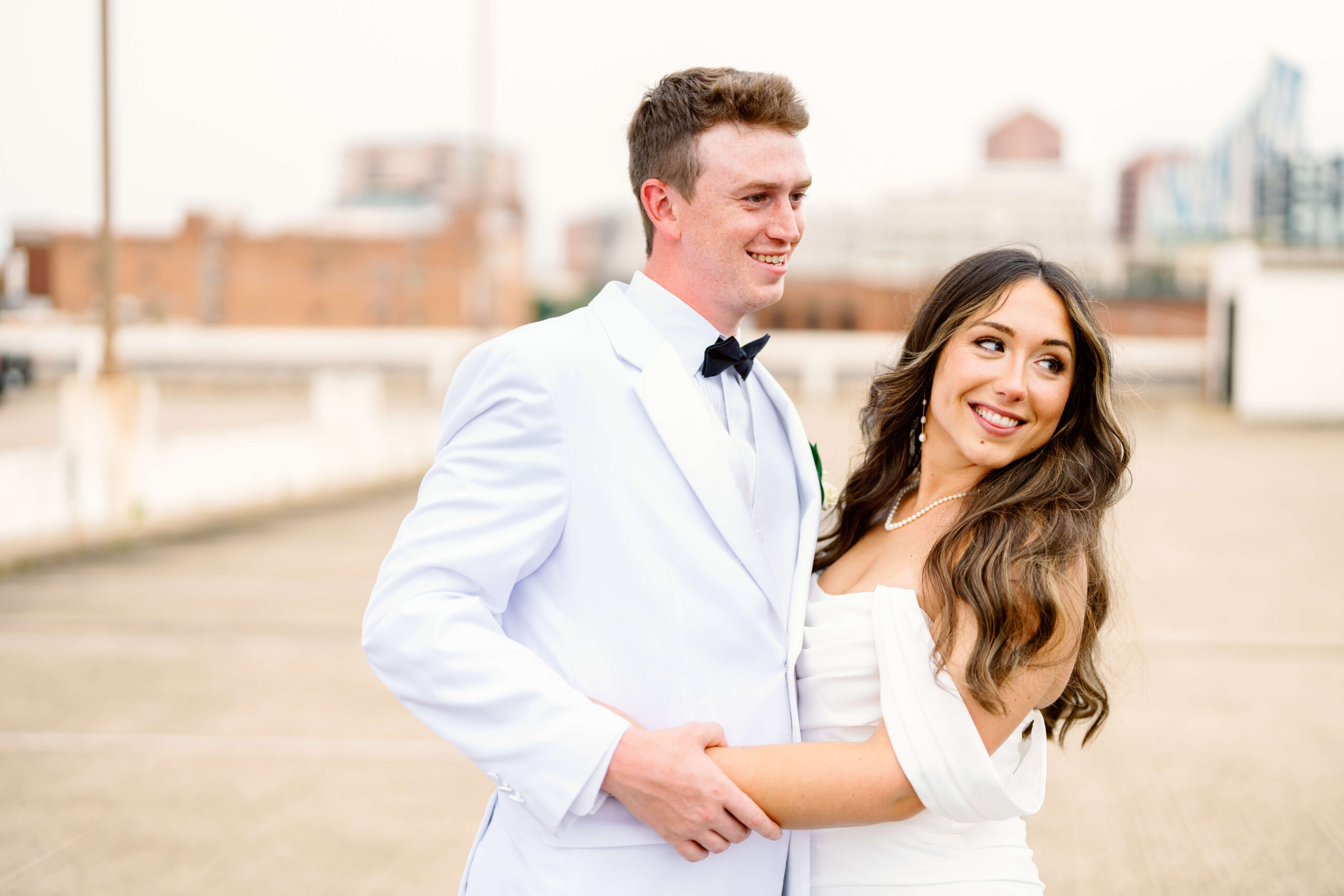 A bride and groom smile while looking over their shoulders on a rooftop