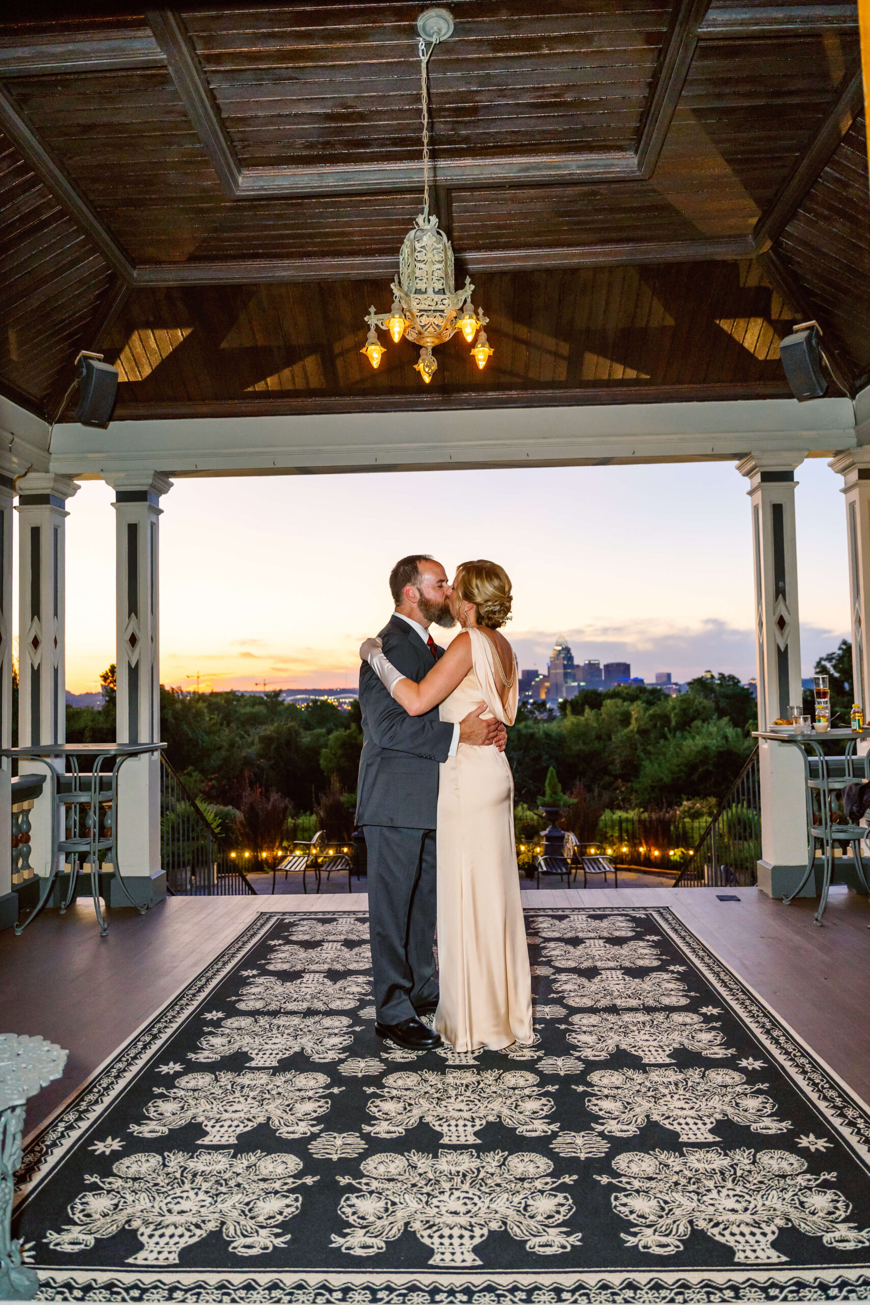 Newlyweds dance and kiss on a porch at sunset at one of the cincinnati wedding venues with a view
