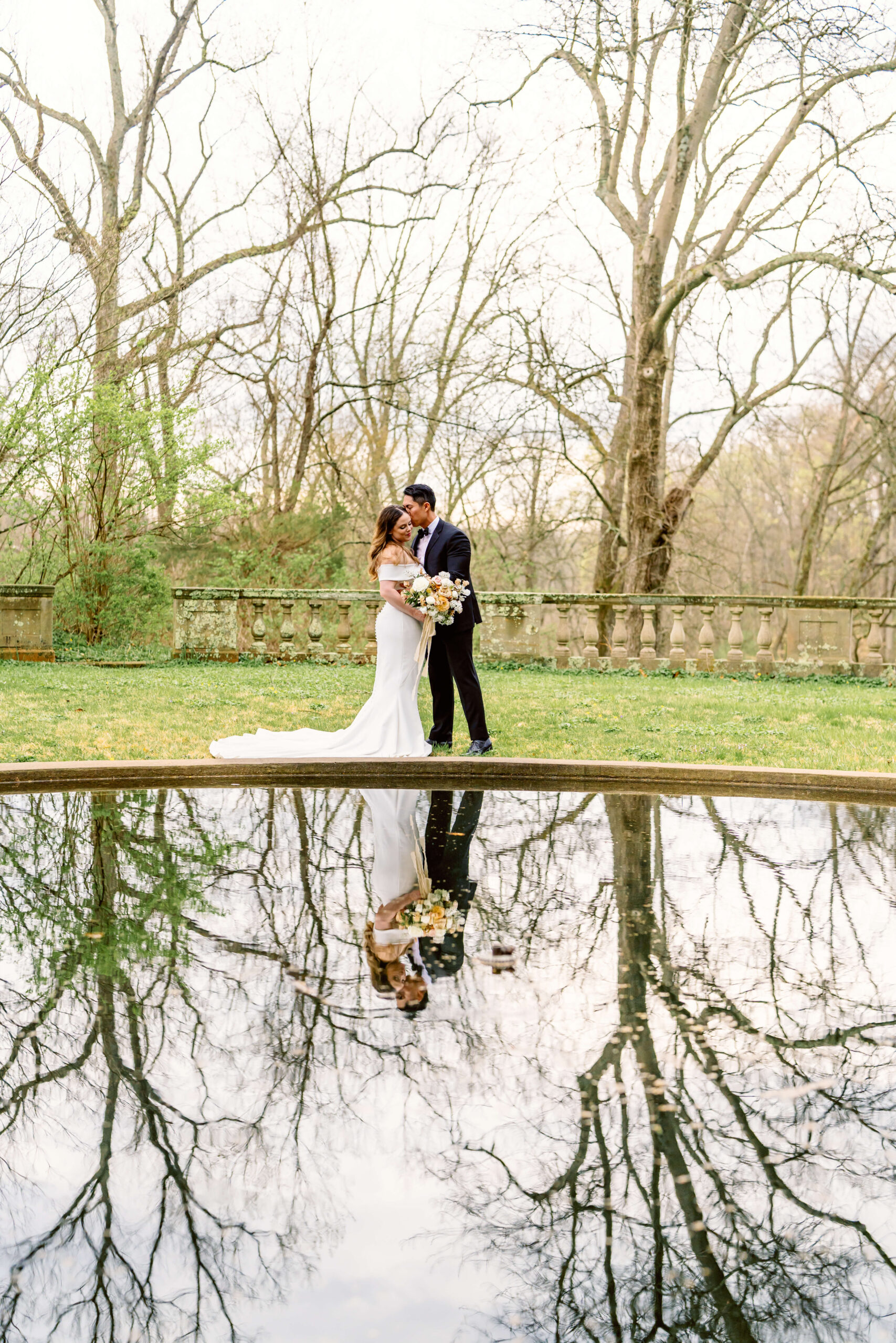 A bride and groom kiss next to a garden pond in early spring
