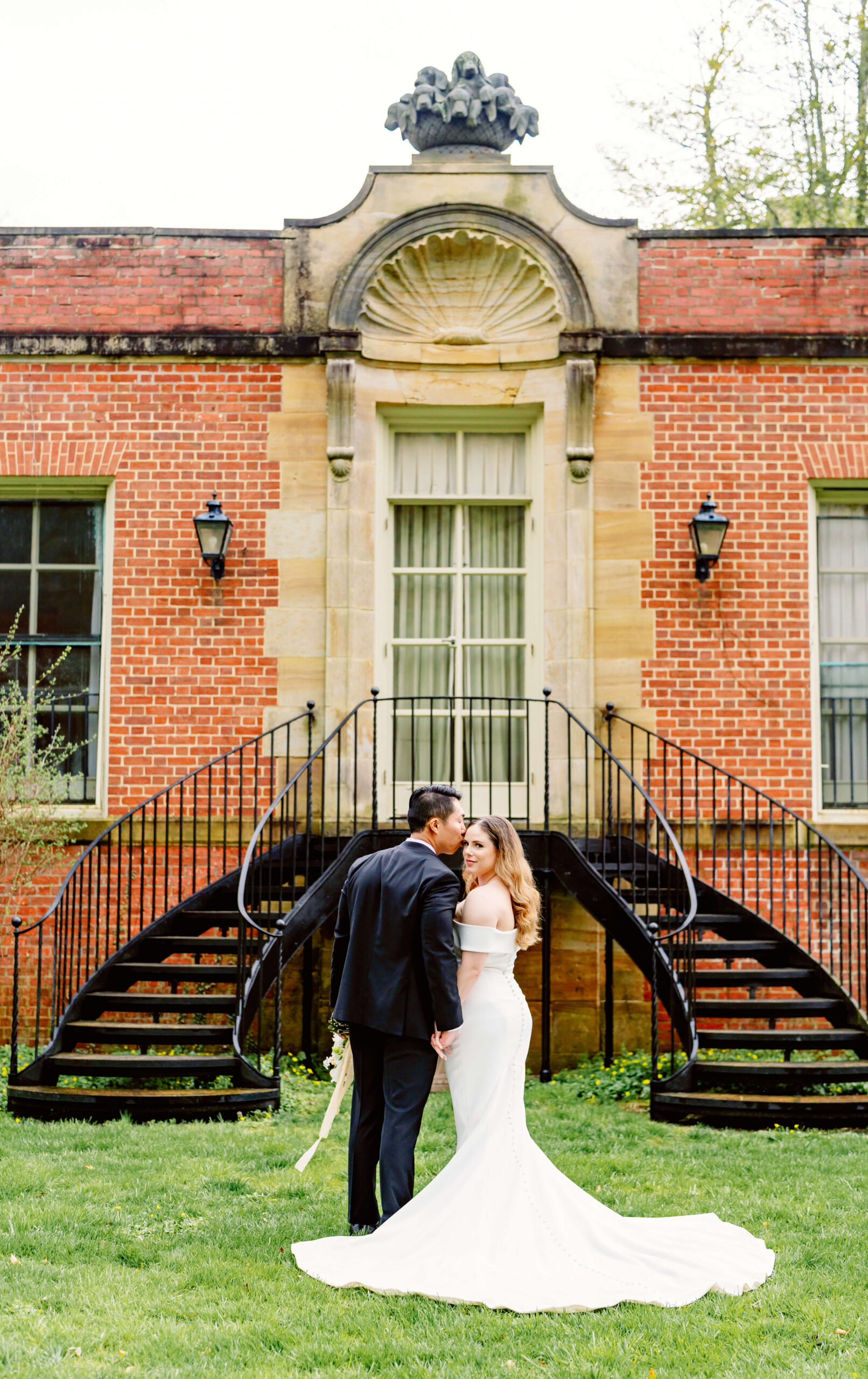 A groom kisses his bride in a lawn in front of iron staircase to one of the estate wedding venues in cincinnati