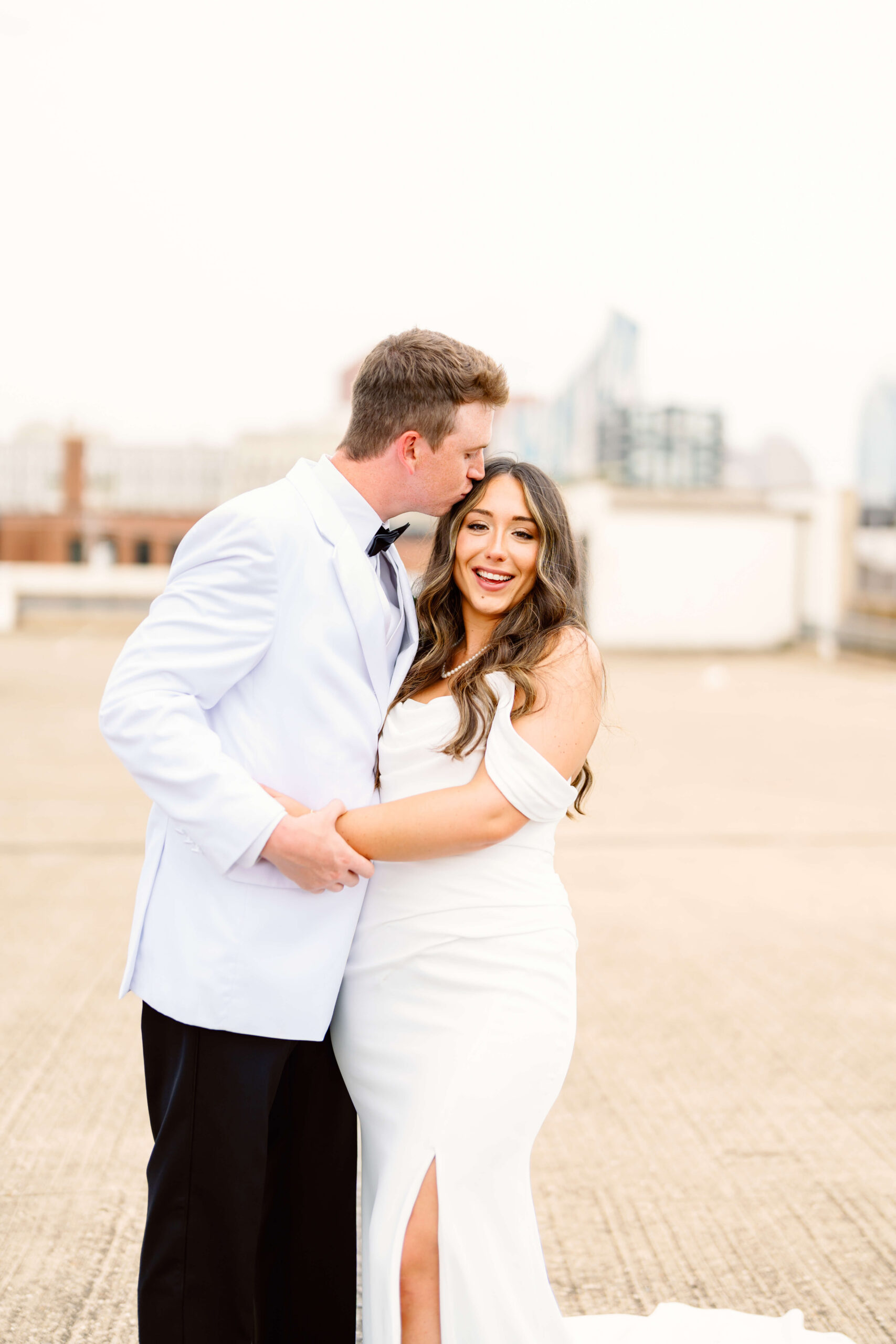 A bride laughs while her groom kisses her head on a rooftop at sunset at one of the unique wedding venues in cincinnati