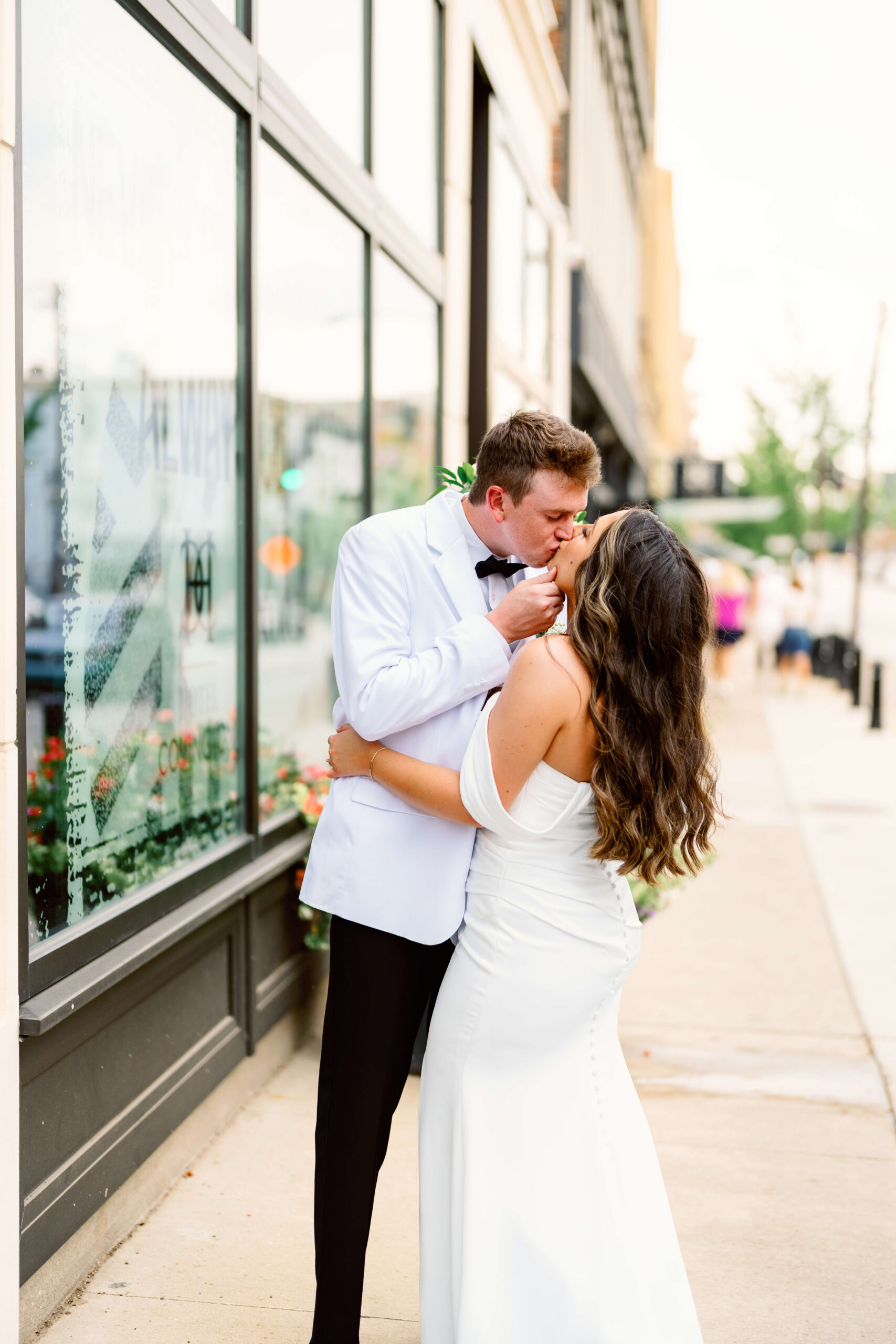 Newlyweds kiss in the sidewalk outside a venue in a white tux and gown