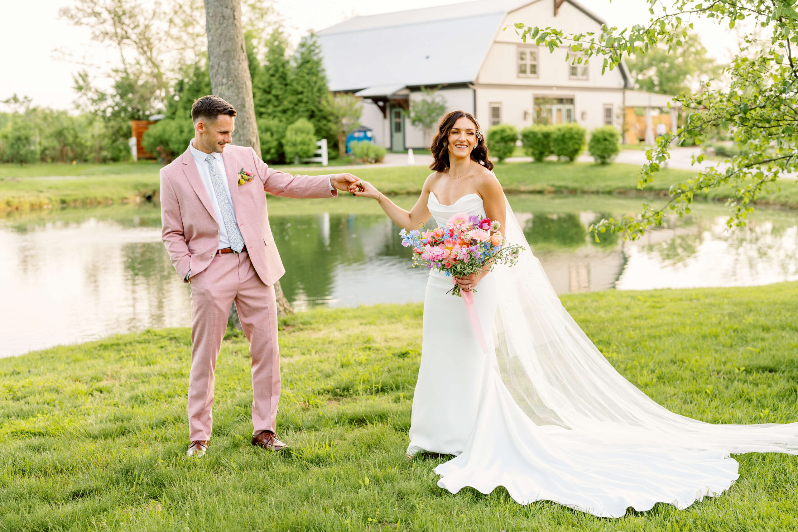 A groom admires his bride in her gown and long veil by a pond at sunset at one of the unique wedding venues in cincinnati