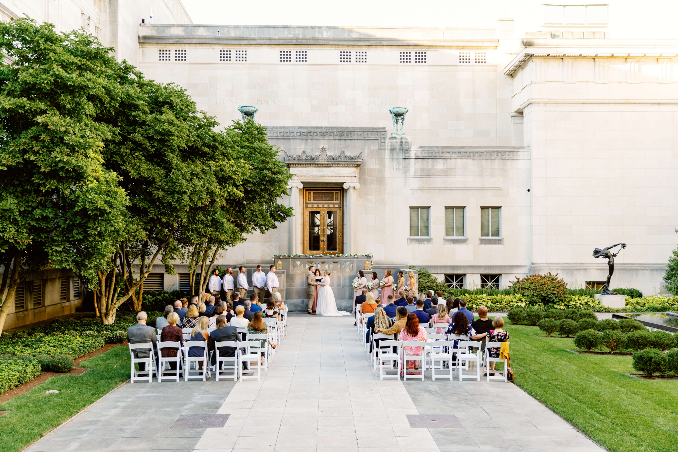 A look down the aisle of one of the unique wedding venues in cincinnati in a lush garden with guests watching and statues