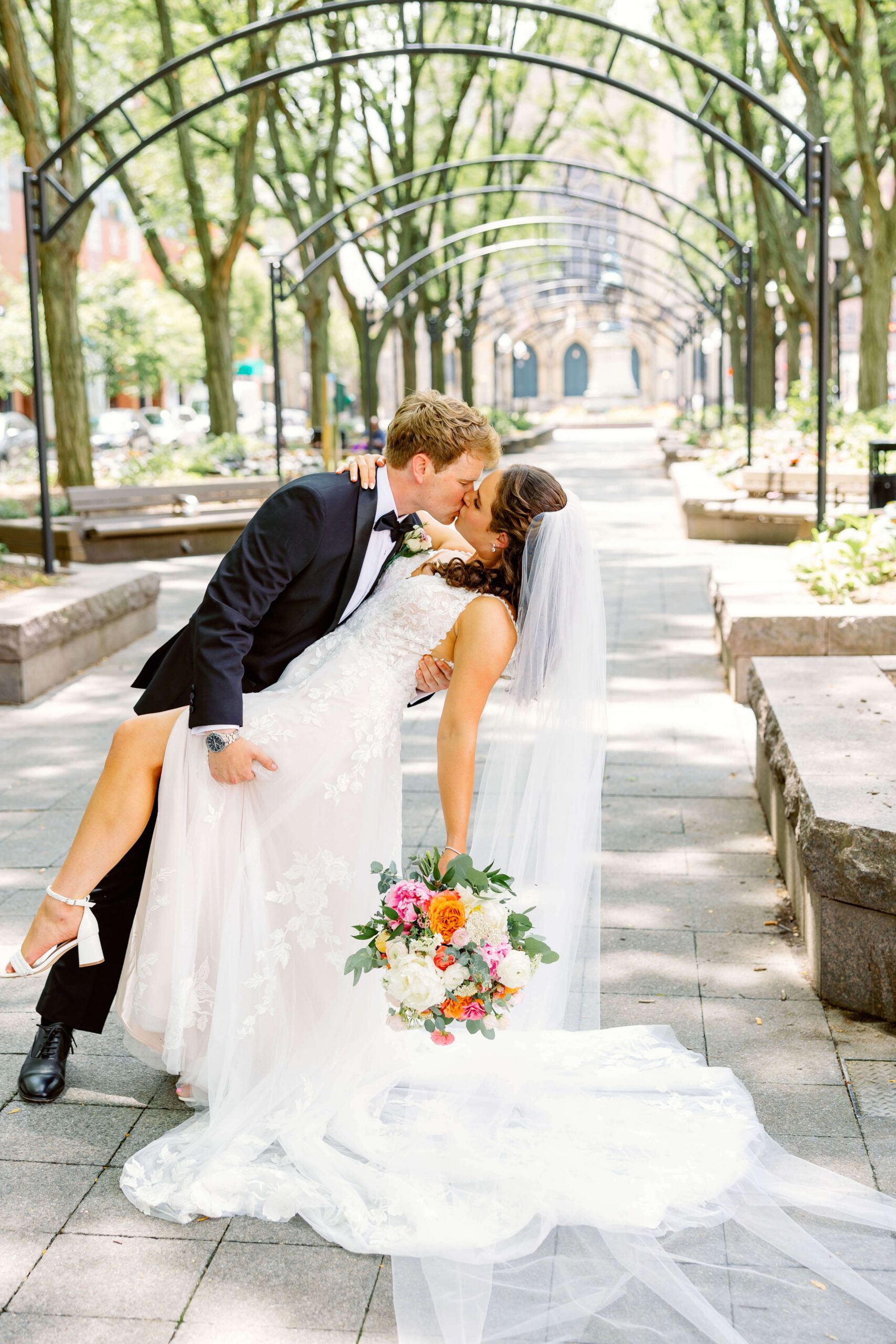 A groom dips his bride a park garden under metal arches for a kiss at one of the unique wedding venues in cincinnati