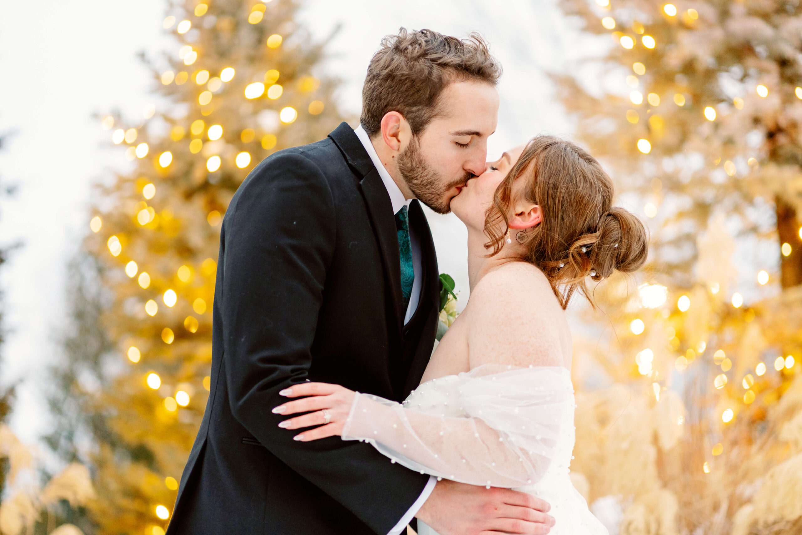 Newlyweds kiss at sunset under twinkling lights in the trees