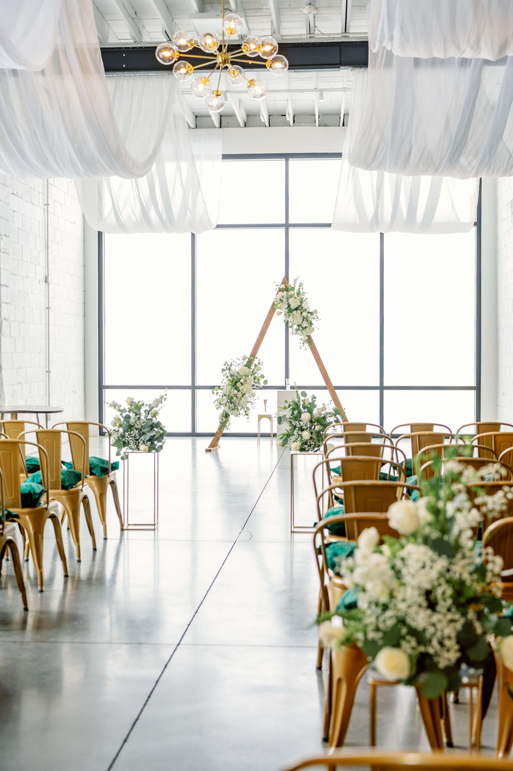 Details down the aisle of white florals and triangle arbor in a white washed brick room at one of the unique wedding venues in cincinnati